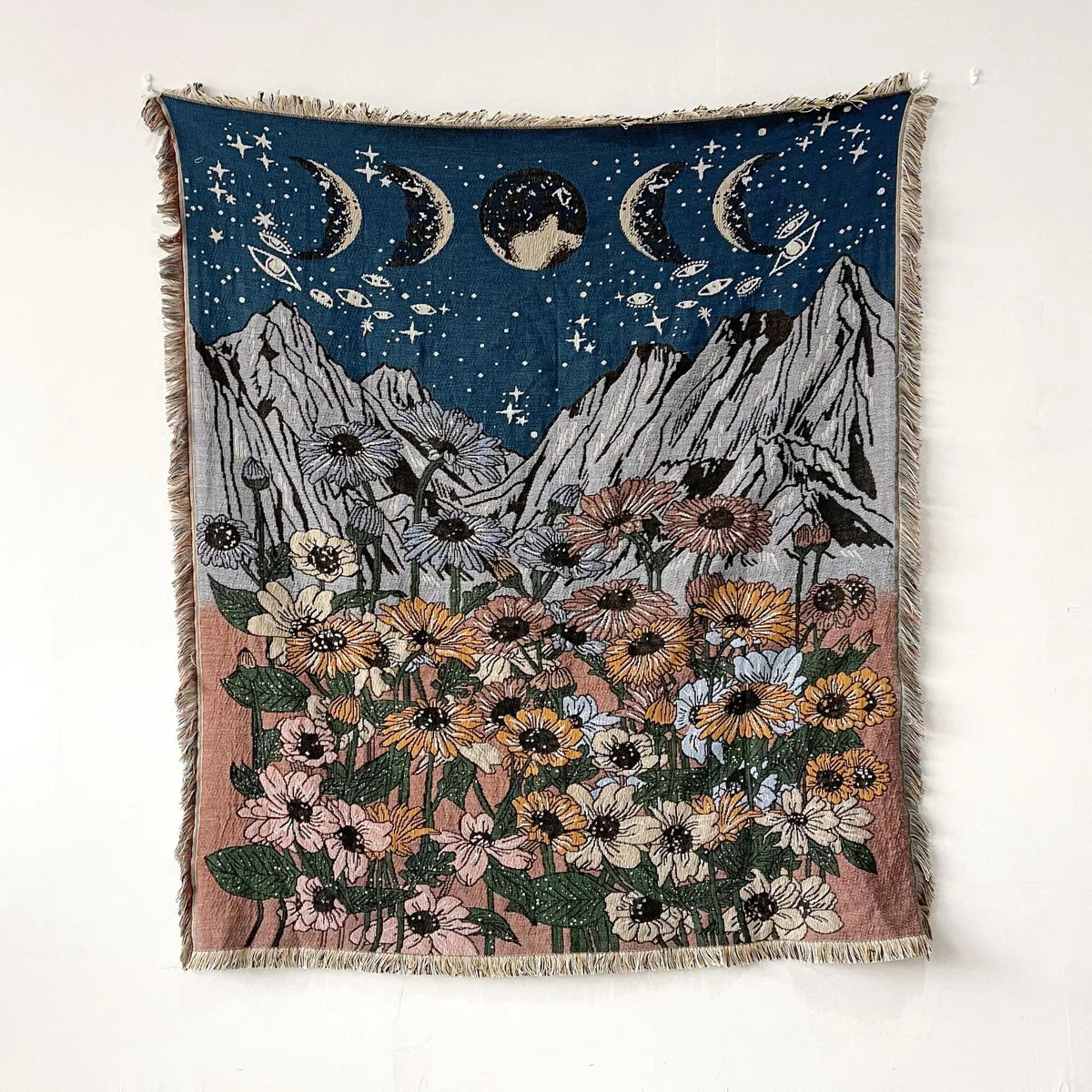A dark blue throw blanket featuring a celestial scene with crescent moons and a field of colorful wildflowers.