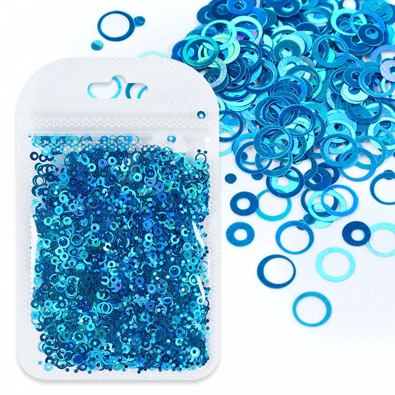 A small white plastic container filled with bright blue sparkly resin glitter circles and loose glitter pieces.