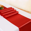 A vibrant red satin table runner is rolled and laid out on a white tablecloth for an event.