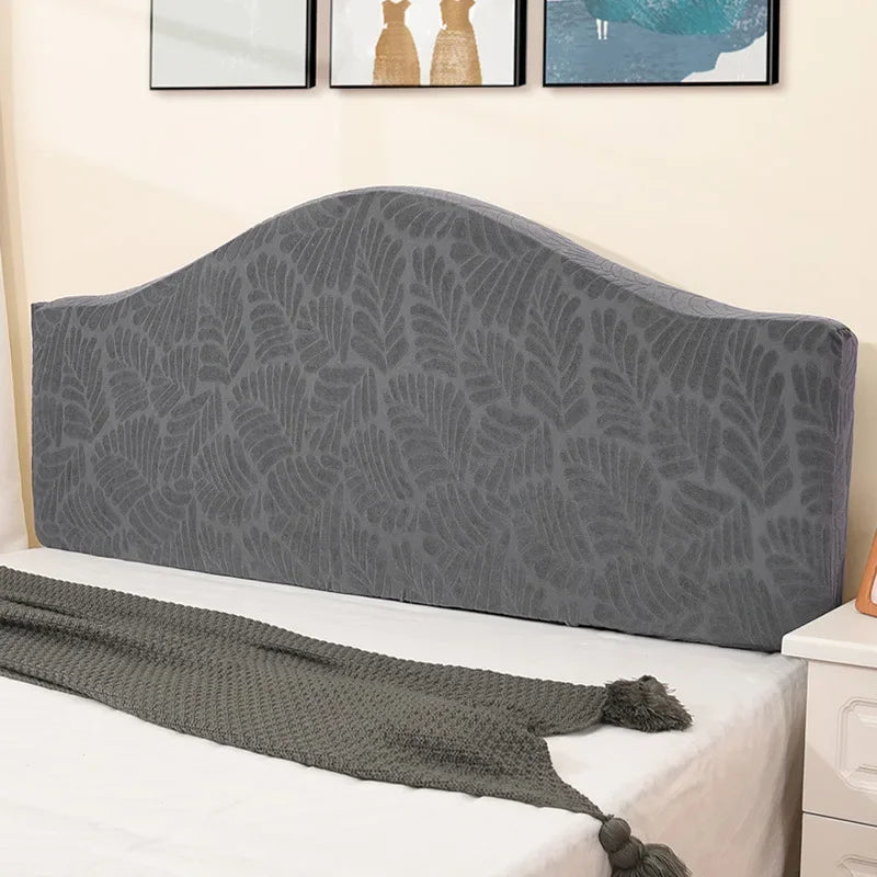 A gray soft elastic headboard cover is displayed on a white bed, with a matching throw blanket draped across it.