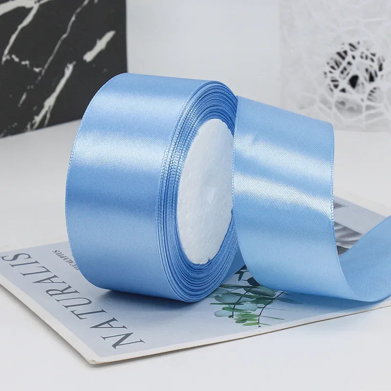 Roll of light blue satin ribbon with white filling shown next to a piece of paper