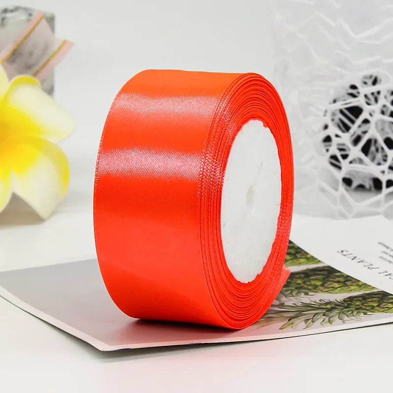 A roll of bright orange satin craft ribbon with a white core, lying on a sheet of paper.