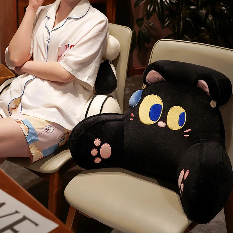 A black animal plush sofa cushion is shown next to a person sitting in a light-colored chair.