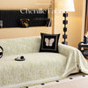 A light green jacquard sofa cover blanket draped over a sofa, with decorative pillows and a lamp in the background.