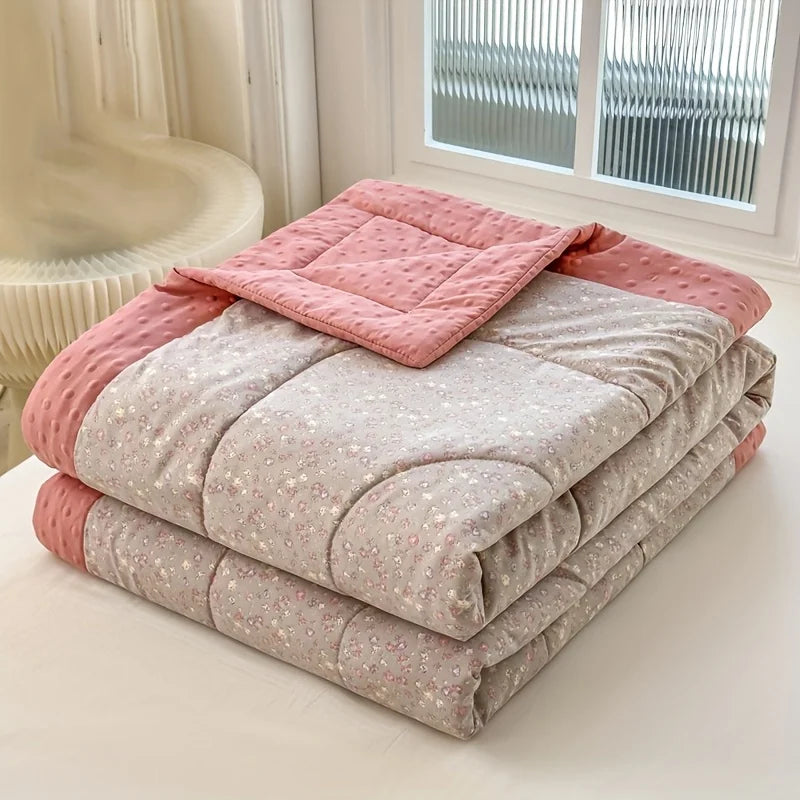 A stack of lightweight floral printed summer quilts in pink and beige tones on a white surface.