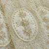 Close-up of beige embroidered sheer fabric featuring delicate floral patterns and pearl beadwork.