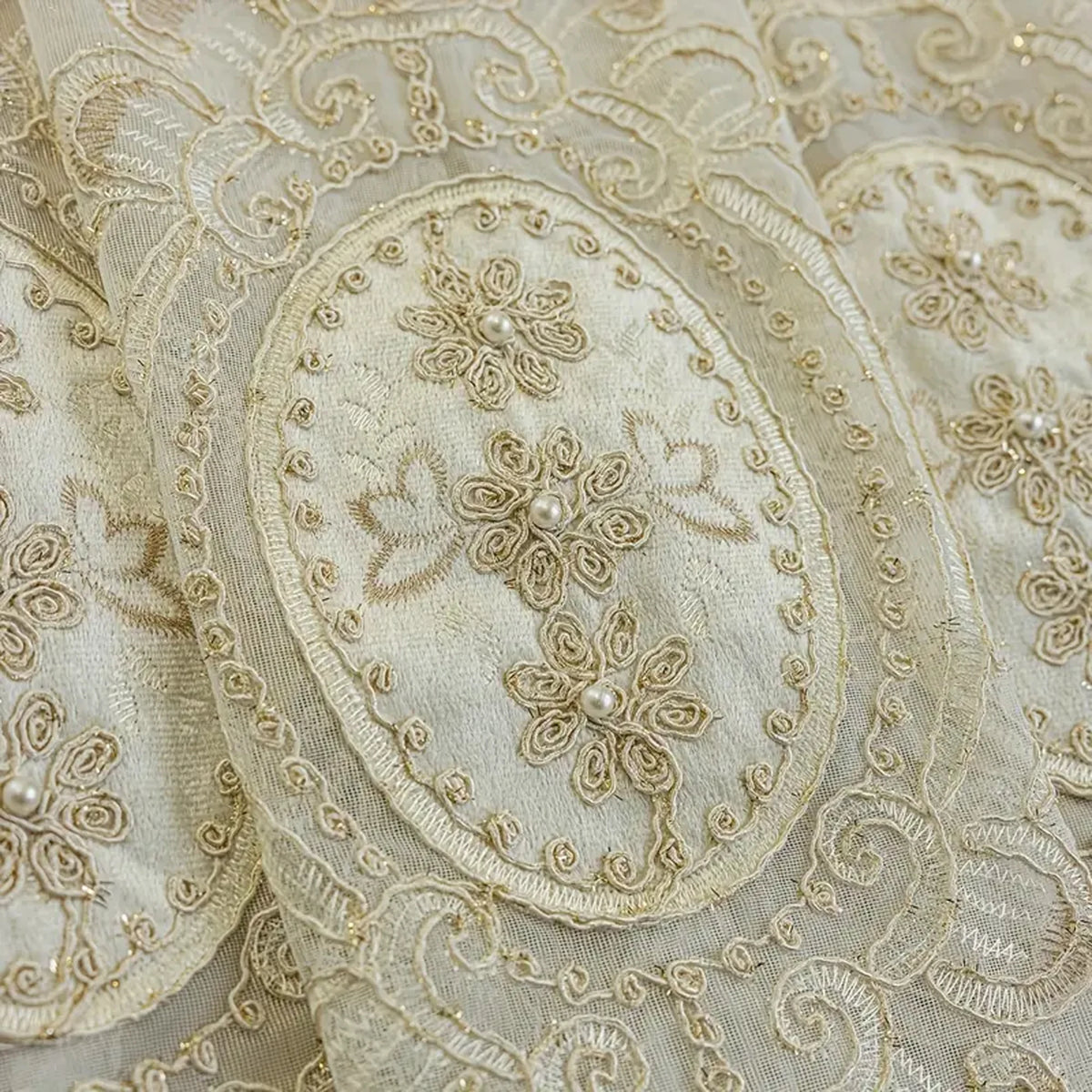 Close-up of beige embroidered sheer fabric featuring delicate floral patterns and pearl beadwork.