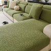 A section of a moss green patterned jacquard sofa cover featuring a branch design and cream accent pillows.