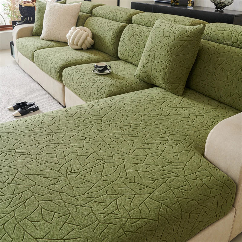 A section of a moss green patterned jacquard sofa cover featuring a branch design and cream accent pillows.