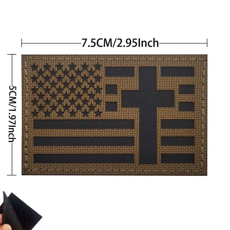 A rectangular embroidered patch featuring a distressed American flag and a cross design on a dark brown fabric.