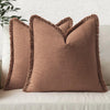 A tan linen throw pillow with a fringed edge resting on a light-colored sofa.