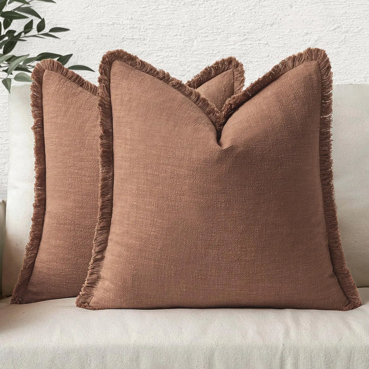 A tan linen throw pillow with a fringed edge resting on a light-colored sofa.