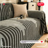 A charcoal sofa cover featuring a herringbone pattern with black and white accents and tassel fringes.