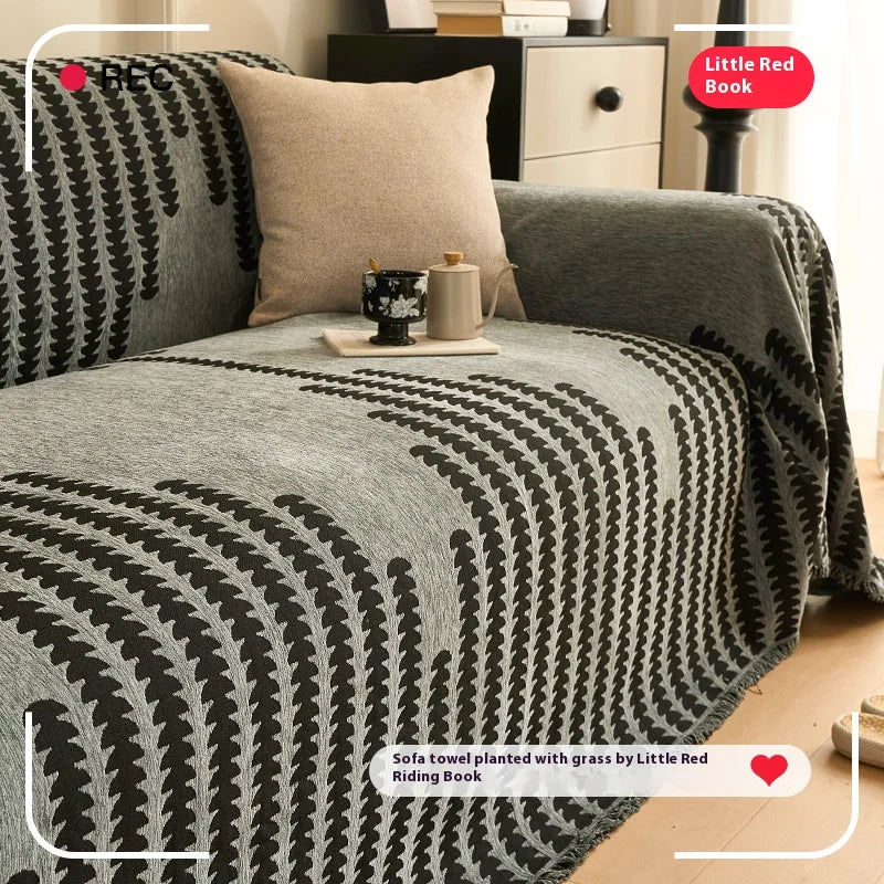 A charcoal sofa cover featuring a herringbone pattern with black and white accents and tassel fringes.