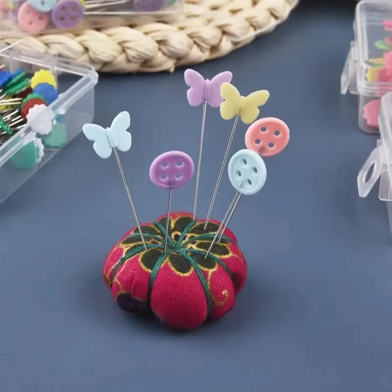 A set of colorful sewing pins shaped like butterflies and buttons arranged on a pink fabric flower.