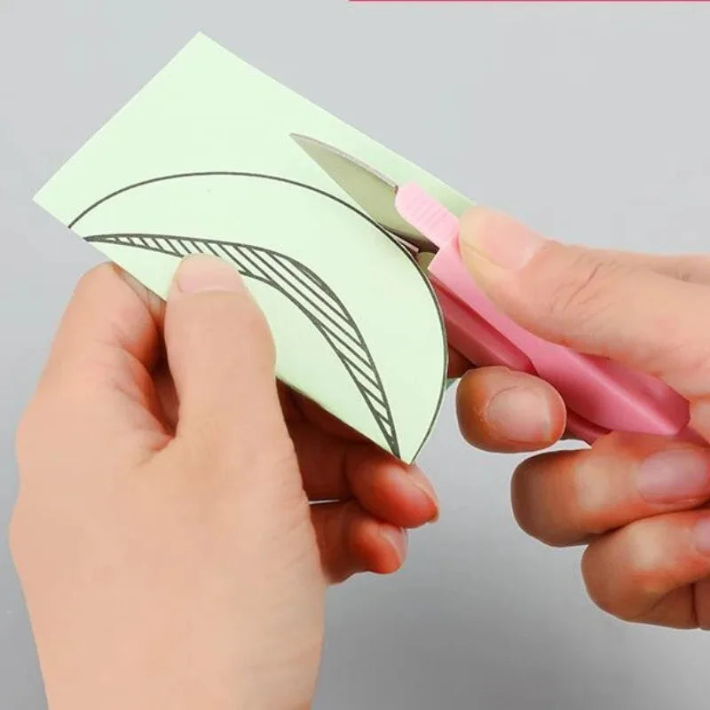A hand is using a pair of pink sewing and embroidery scissors to cut a curved line on a light green piece of fabric.