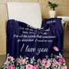 A dark blue throw blanket with pink floral embroidery is draped over a chair.