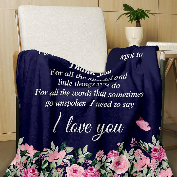 A dark blue throw blanket with pink floral embroidery is draped over a chair.