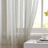 A white sheer curtain with a rod pocket is drawn partially over a window in a bright room.