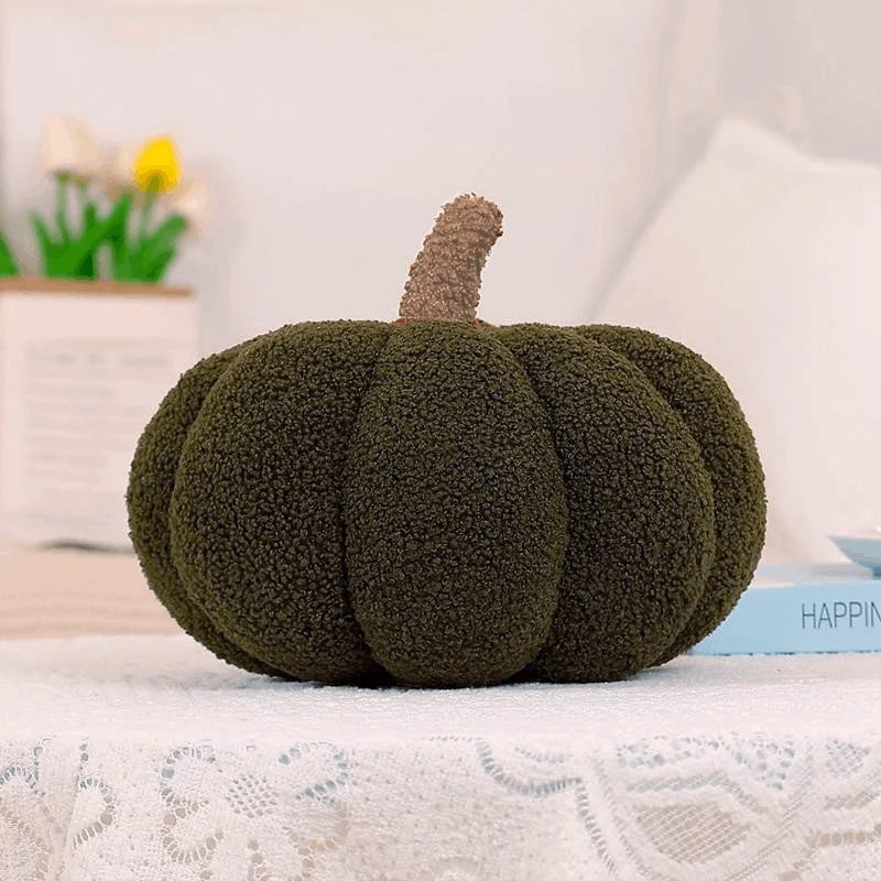 A textured, olive green 3D pumpkin shaped throw pillow with a brown stem, displayed on a white lace tablecloth.