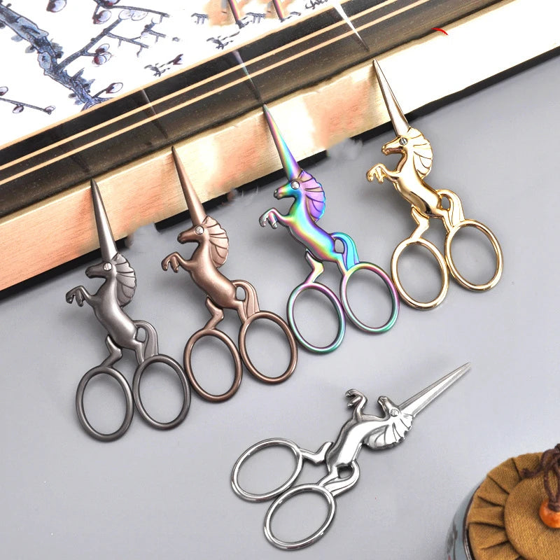 A set of three-color stainless steel unicorn sewing scissors resting on a wooden surface.