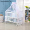 White crib with a sheer mosquito net covering, displayed in a brightly lit room.