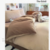 A beige quilt bedding set with a brown duvet and pillows on a bed, next to a lamp and a camera.