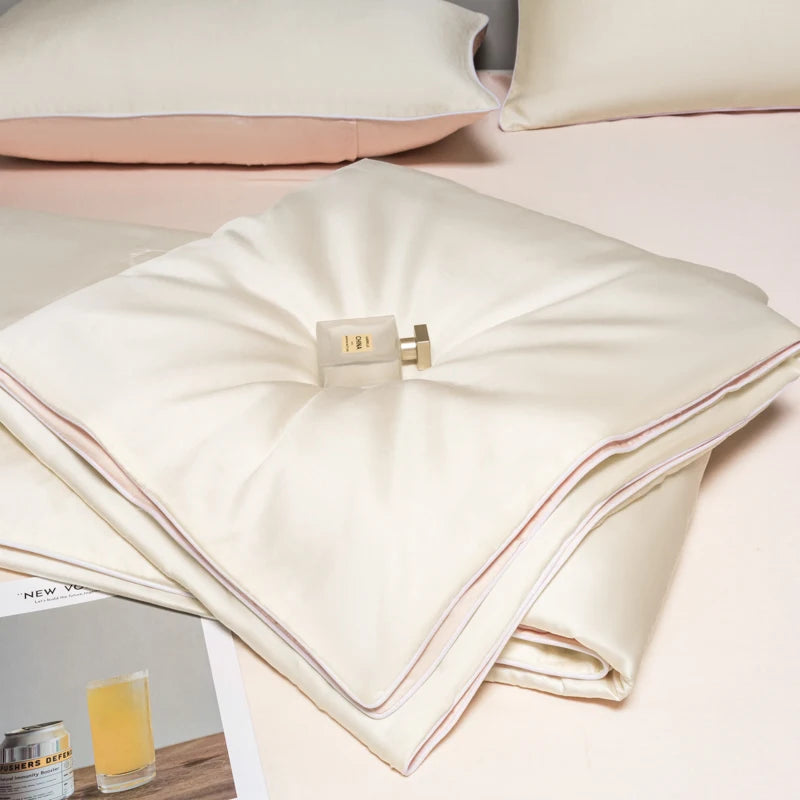 White ice silk cooling quilt folded on a pink surface with a glass of juice nearby.