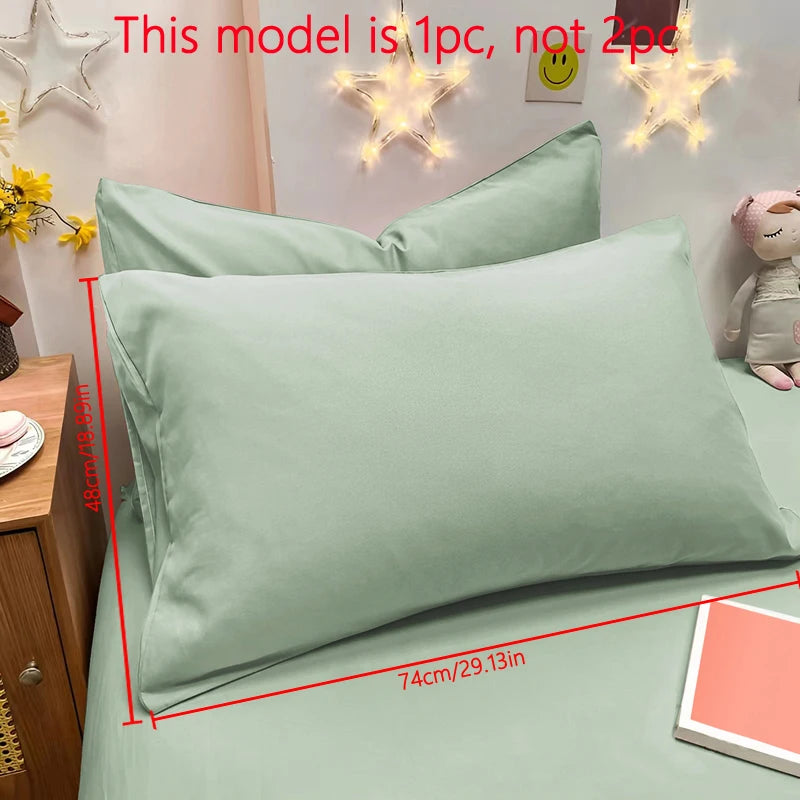 A single matte sage green pillowcase is displayed on a bed, with decorative star lights in the background.