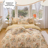 A beige floral cotton duvet cover and pillow set displayed on a bed with sheer curtains.