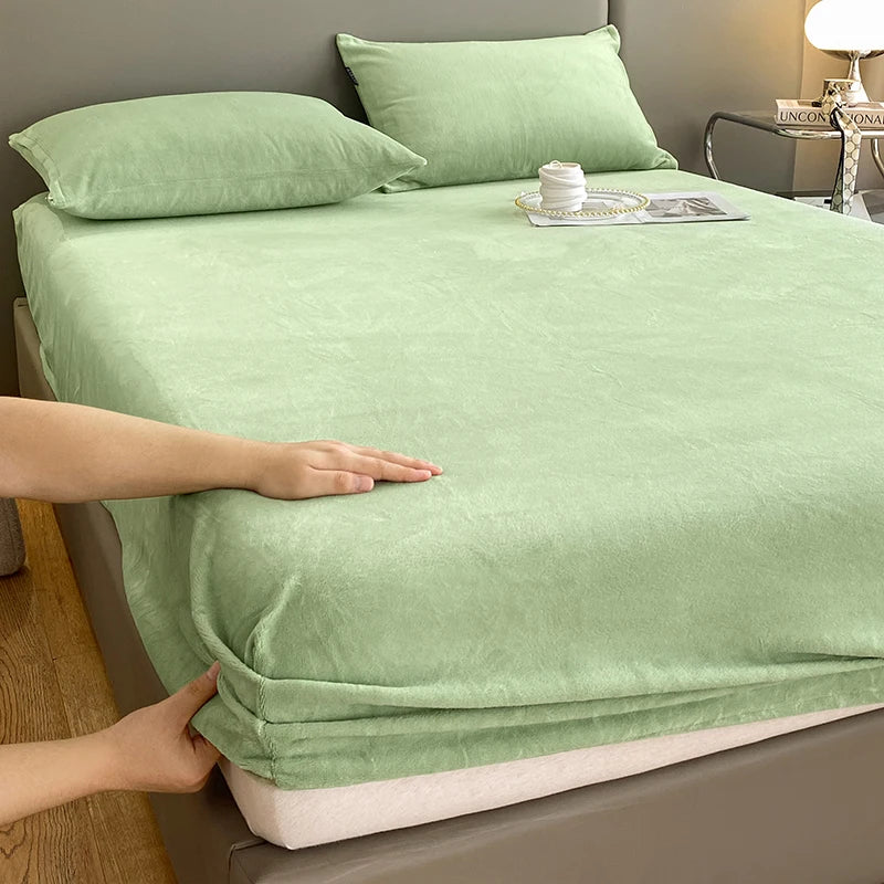A hand is adjusting a light green luxury velvet bedding set on a bed.