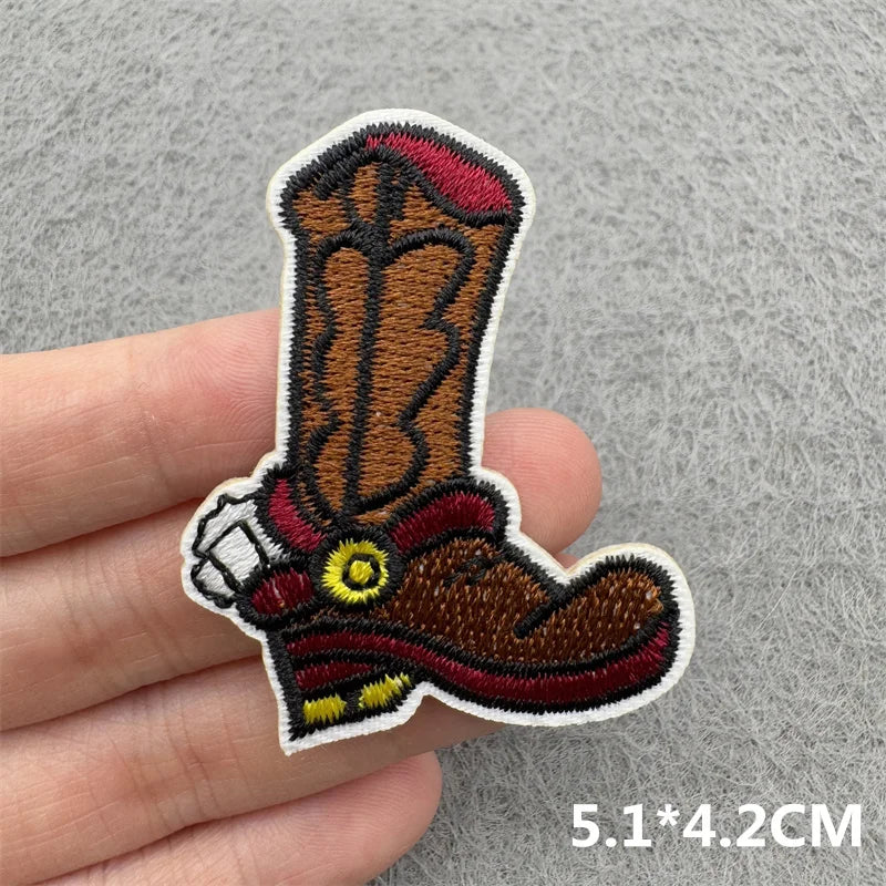 An embroidered patch of a brown cowboy boot with red and yellow detailing on a hand.