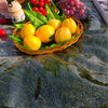 A woven basket filled with yellow lemons and green leaves placed on a dark, textured cloth.