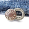 Silver oval button with the text FASHION JEANS embossed on it, resting on a denim fabric.