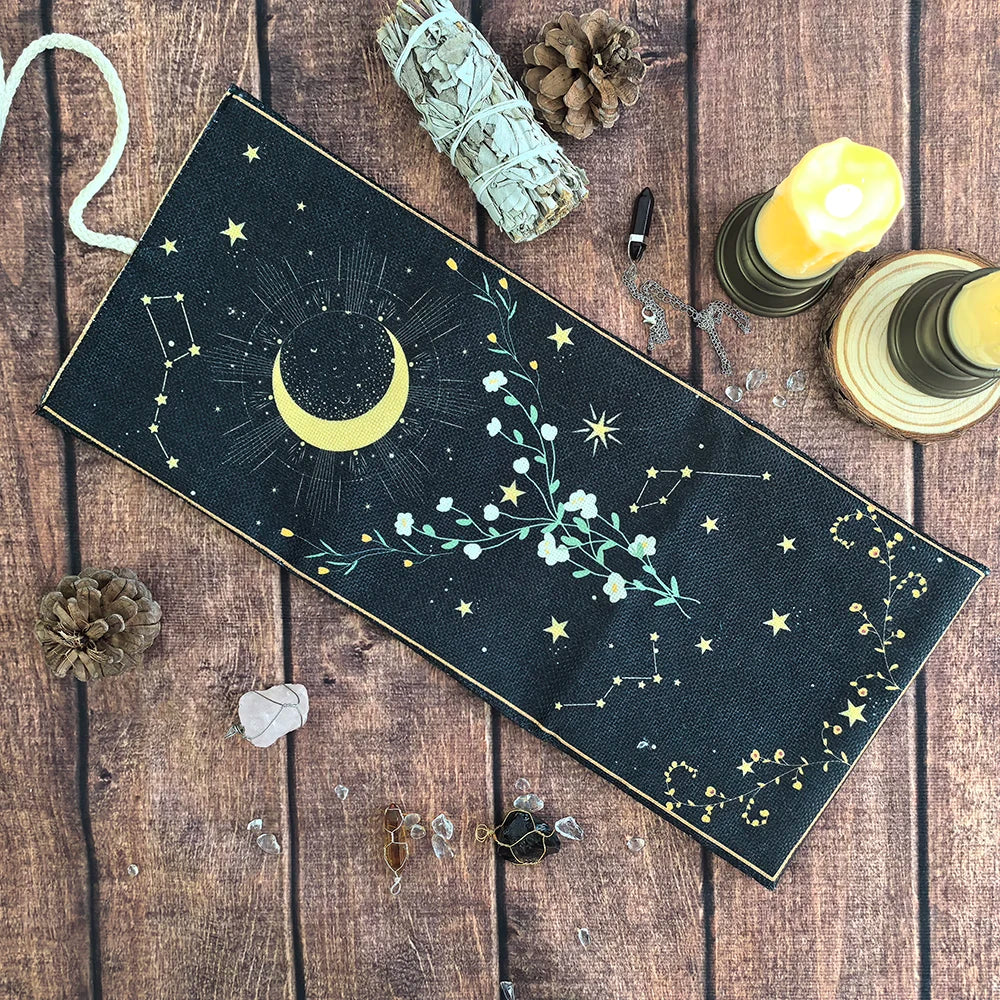 A dark fabric pouch decorated with a celestial theme featuring a crescent moon, stars, and floral elements, resting on a wood
