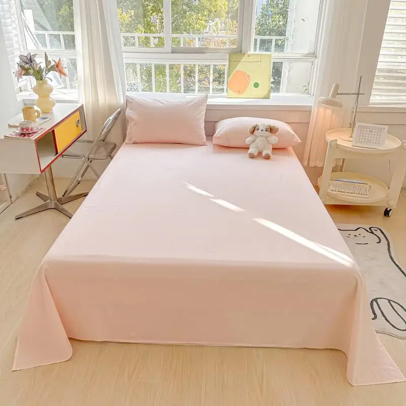 A pink organic cotton bedding set featuring a flat sheet and pillows is displayed on a bed in a bright room.
