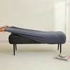 A dark gray elastic jacquard bench cover is shown on a black upholstered bench in a bright room.