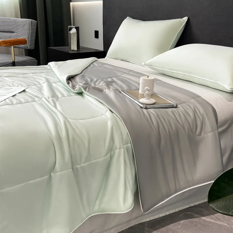 A light green reversible cooling quilt is displayed on a bed with gray bedding and pillows.