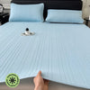 Light blue cooling ice silk bed pad placed on a bed with dark gray bedding and pillows.