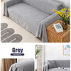 A grey waterproof sofa cover draped over a modern sofa, displayed on a light rug and next to a wooden box.