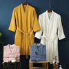 A yellow cotton terry robe and a white cotton terry robe are displayed hanging against a dark blue wall.