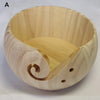 A light-colored wooden bowl with a spiral design used for yarn and fiber organization.
