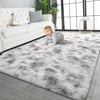 A fluffy gray plush carpet is spread on a floor in front of a white leather sofa and large windows.