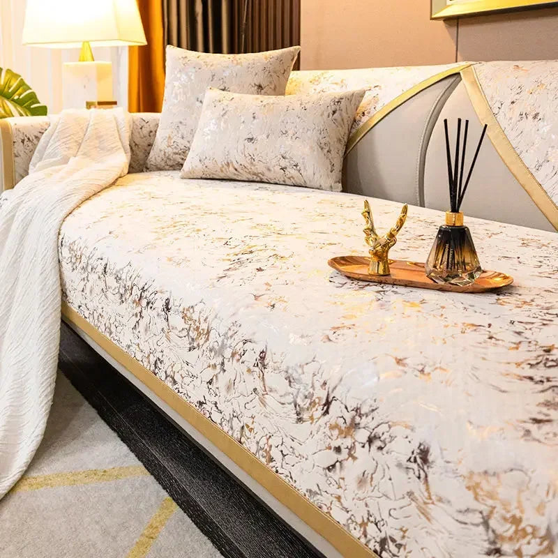 A luxury velvet sofa cover featuring a light cream background with gold leaf accents and white pillows.