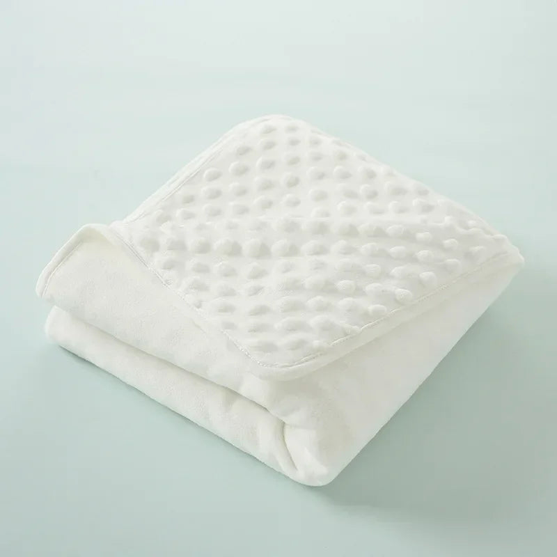 A white, quilted baby name swaddle blanket folded neatly on a light blue surface.