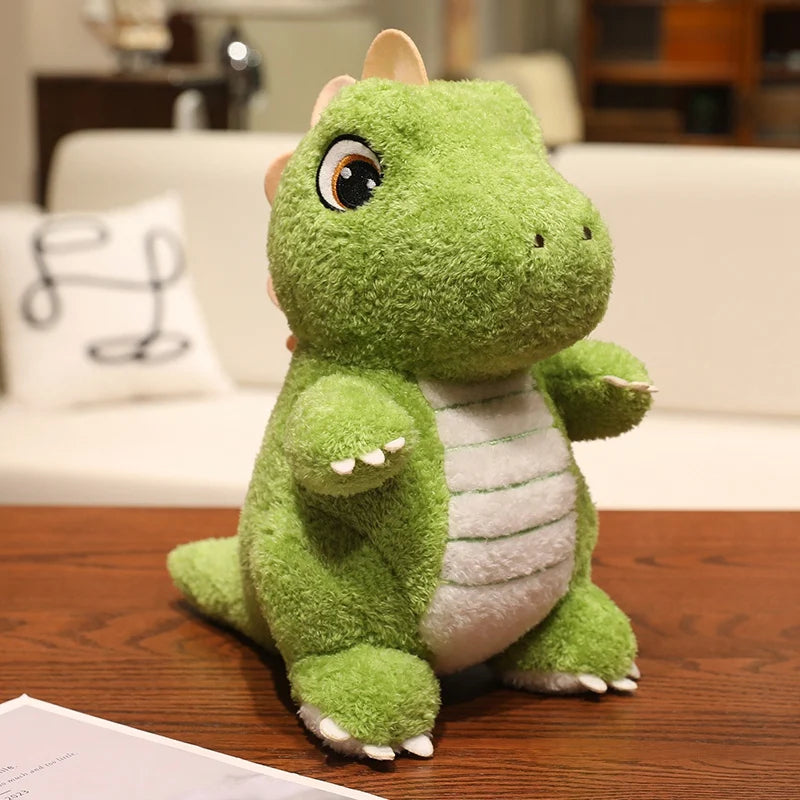 A cute green dinosaur plush toy with large eyes and a white belly sitting on a wooden surface.
