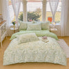 A light green floral duvet cover and pillow set displayed on a bed in a bright room with white curtains.