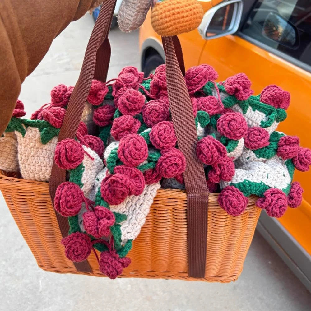 A bouquet of handmade rose crochet blankets in various shades of red, green, and cream inside a woven basket.