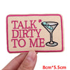 Pink embroidered patch with the text TALK DIRTY TO ME on a beige fabric background