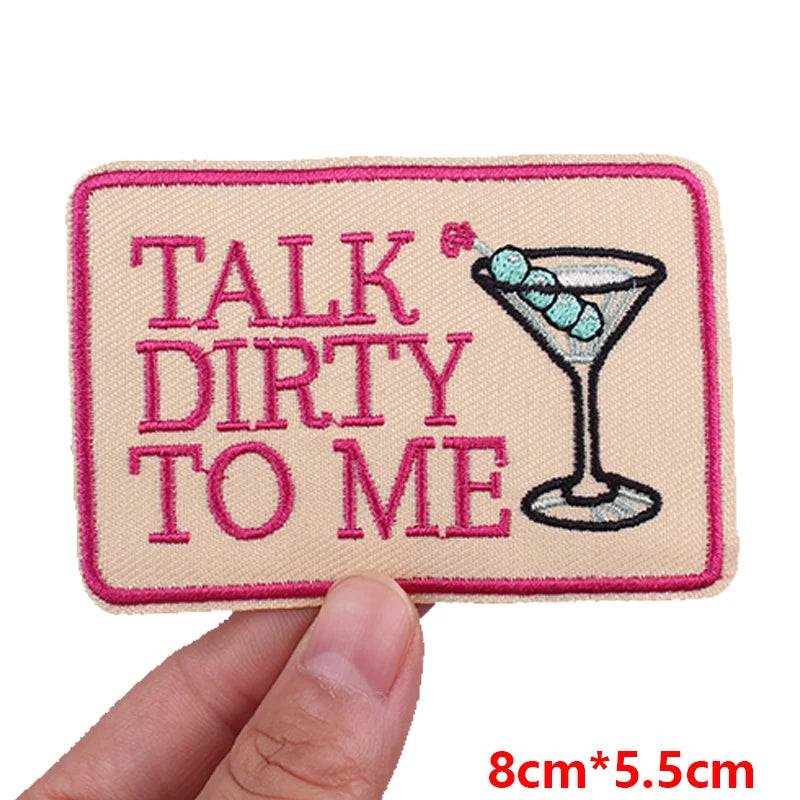 Pink letter embroidered iron-on patch with text 'Talk Dirty to Me' on a beige fabric background